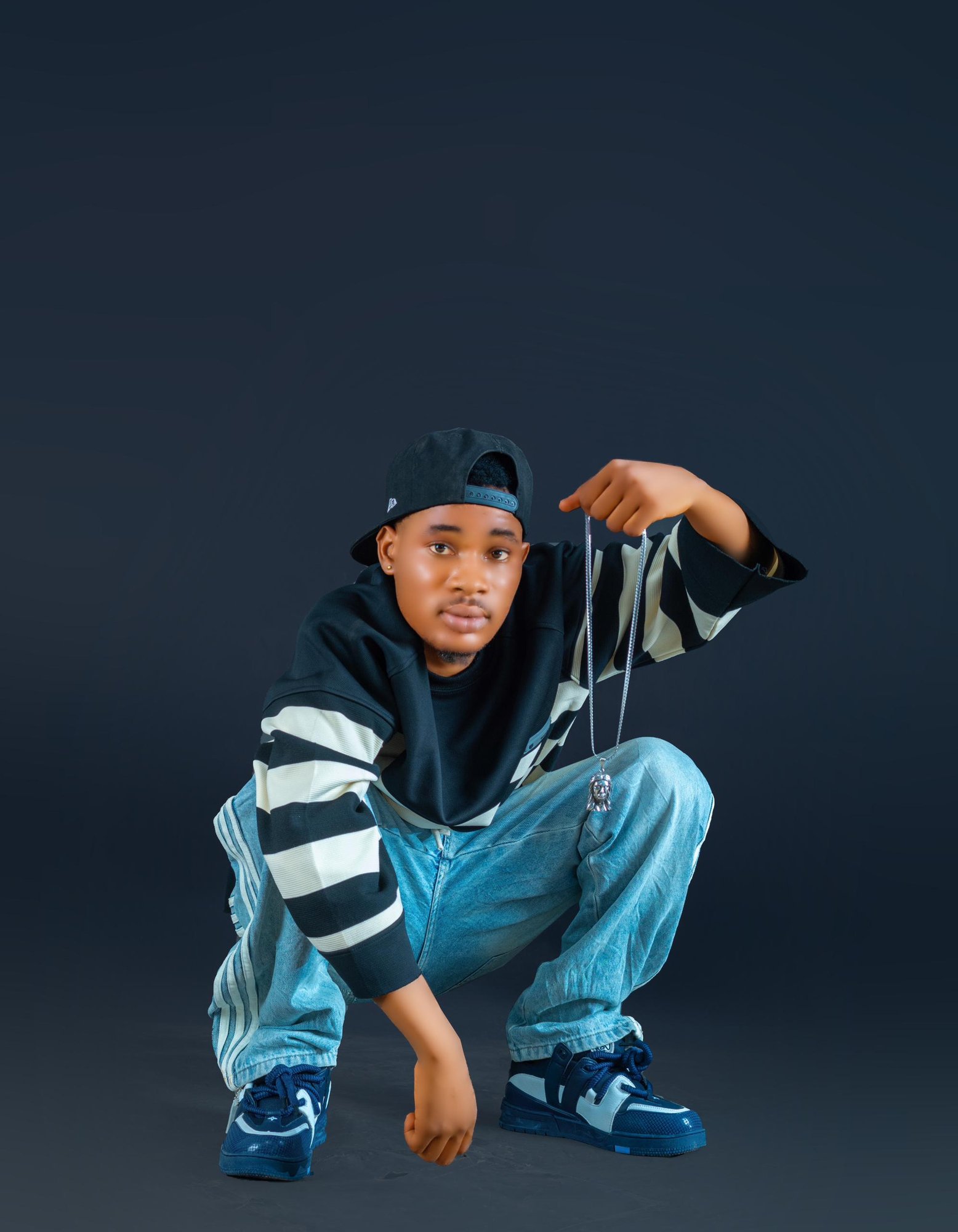 Bhay Rapper crouching in a striped hoodie, holding a silver chain, studio portrait